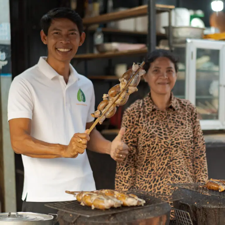 Siem Reap street food tour leader, a local chef with international hotel experience, holding grilled Cambodian BBQ frog